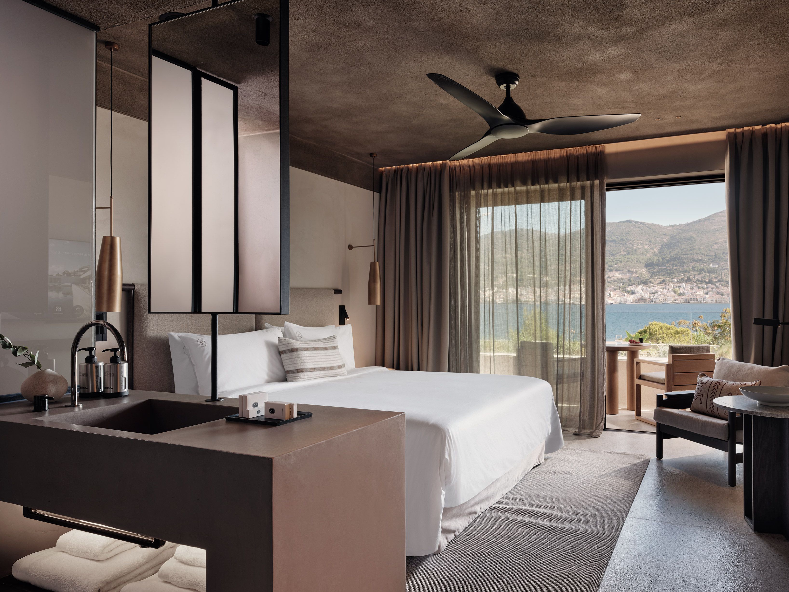 A modern hotel room with a large bed, a bathroom with a sink and mirror, and a view of the sea.