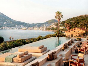 An infinity pool with lounge chairs and a view of a coastal town. - Nirema Hotel & Spa Samos - MGallery Collection (opening Q3 2026) (Samos)