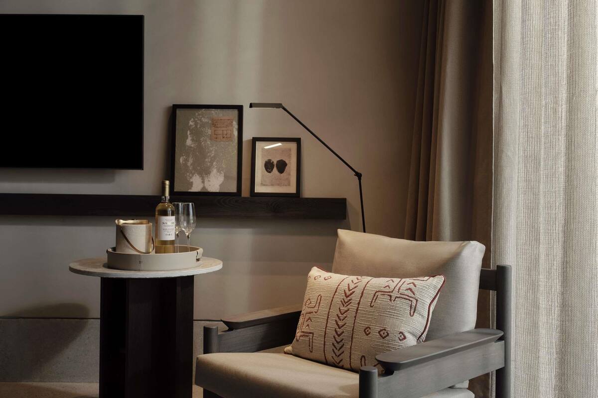 Et moderne værelse med en sofa, et lille rundt bord med en flaske og glas, en gulvlampe og et billede på væggen.