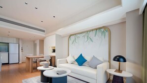 Un salon moderne avec un canapé blanc, des coussins bleus et gris, une table basse ronde et une table d’appoint avec une lampe.