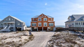 Una proprietà fronte spiaggia con una casa centrale, due edifici laterali e un sentiero sabbioso che conduce alla spiaggia.