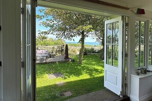 A door leading to a garden with a view of the sea, a wooden bench, and a small table. - Norfolk Seaview Luxury Retreat With 7 Bedrooms (Norwich)