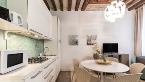 Een moderne keuken met witte kasten, een magnetron en een gasfornuis. Er is een eethoek met een ronde tafel en rieten stoelen.