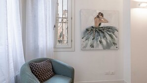 Een kamer met een raam, een schilderij van een ballerina, een teal fauteuil en een bed.