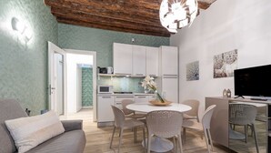 Een moderne woonkamer met een bank, eettafel, stoelen en een keuken met kasten en apparatuur.