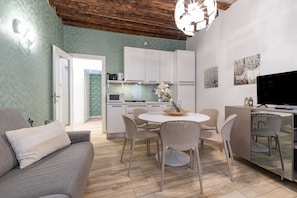 A modern living room with a sofa, dining table, chairs, and a kitchen area with cabinets and appliances. - Domus Rialto Emerald- Bright 2 Bedrooms in Central (Venice)