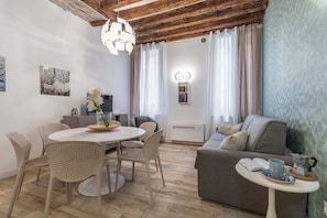 A cozy living room with a round dining table, chairs, a sofa, and a small side table with a cup and book. - Domus Rialto Emerald- Bright 2 Bedrooms in Central (Venice)