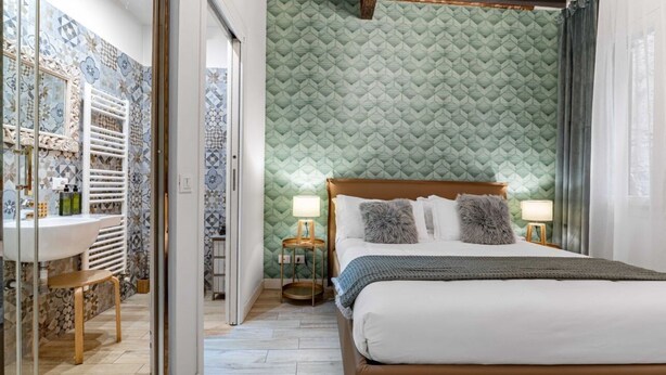 Een slaapkamer met een bed, bedlampen, een nachtkastje, een spiegel, en een badkamer met een wastafel en toilet.