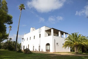 Un bâtiment blanc doté d’un toit plat, de nombreuses fenêtres et d’un grand rocher au premier plan.