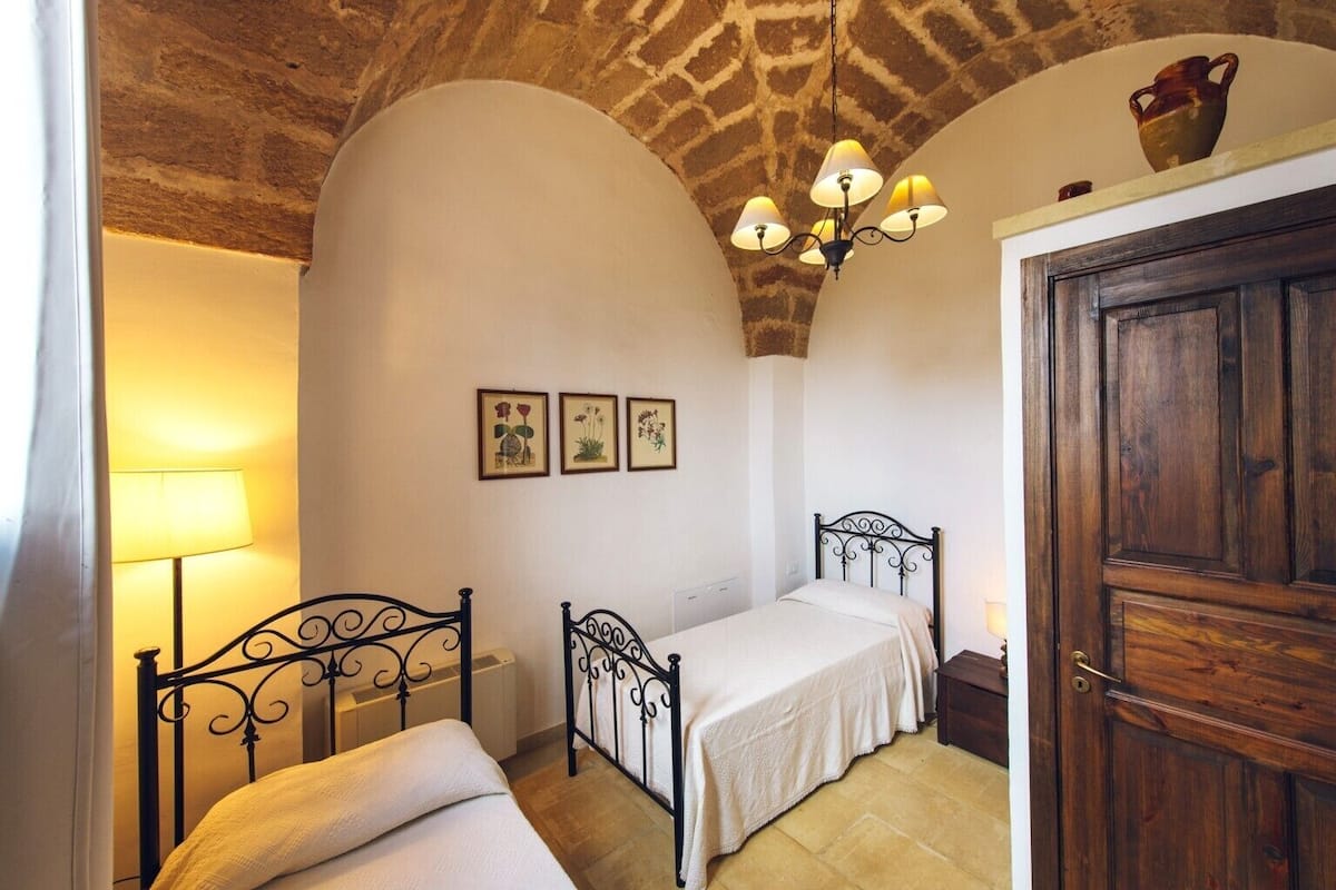 A bedroom with a bed, a lamp, a wooden door, and a stone ceiling.