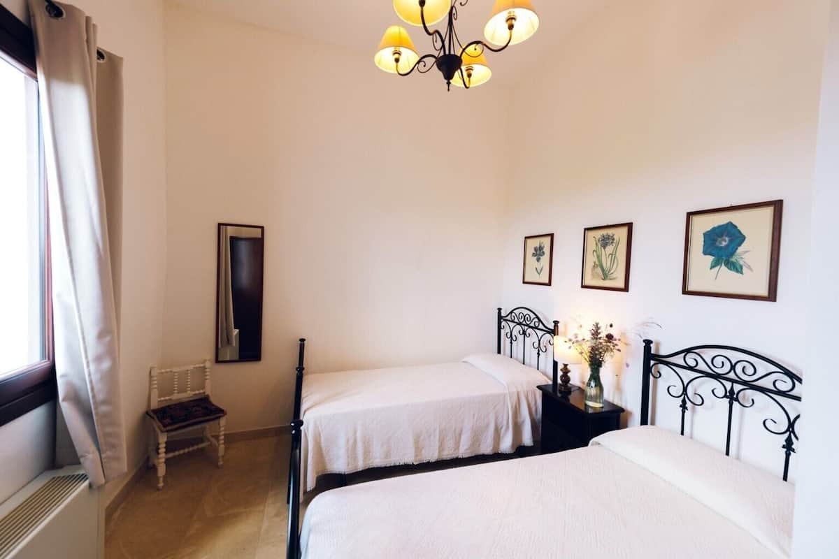 A room with two beds, a chair, a mirror, and a chandelier.