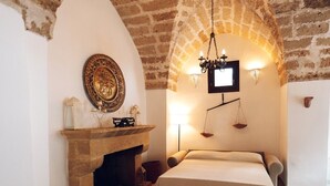 Ein Zimmer mit Kamin aus Stein, einem Bett mit beiger Bettdecke, einer Kristallleuchtre und einer an der Wand montierten Waage.