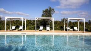 Ein klares Schwimmbecken mit weißen Liegestühlen unter Pergolen.