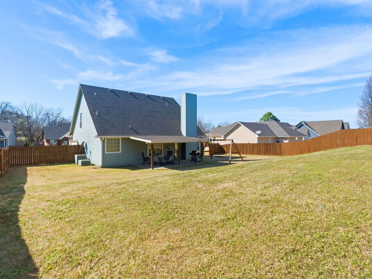 A residential house with a covered patio, a fenced yard, and a neighboring building.