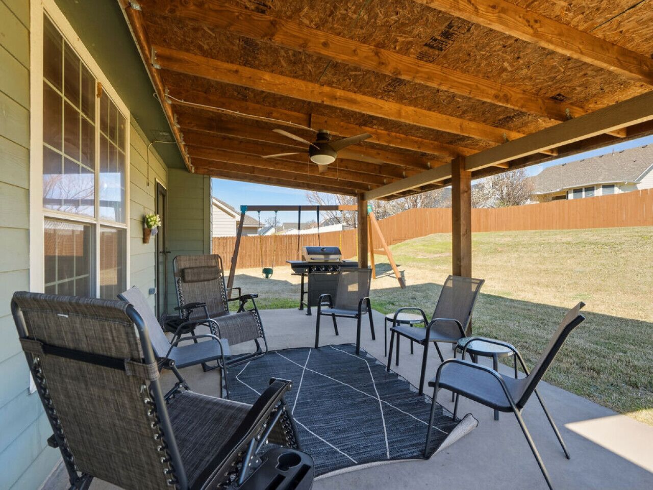 A covered patio with outdoor furniture, a grill, and a ceiling fan.