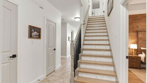 A staircase leading to a bedroom with a wooden floor and a nightstand with a lamp. - Emily House | 3 King Beds | Pet Friendly (Ada)