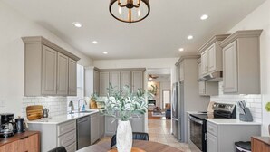 A modern kitchen with grey cabinets, a round dining table with chairs, and a vase with plants. - Emily House | 3 King Beds | Pet Friendly (Ada)