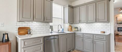 A kitchen with grey cabinets, a dishwasher, a sink, and a wooden cutting board.