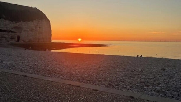 Una spiaggia con un'imponente formazione rocciosa e un tramonto.