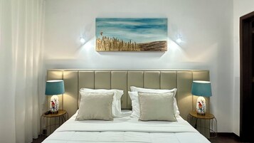 Quarto de hotel com uma cama grande, duas mesas de cabeceira com abajures, um quadro na parede e uma janela com cortinas.