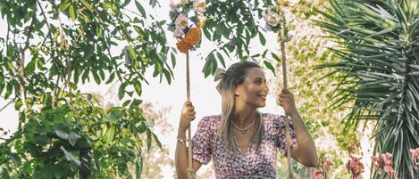 A person sitting on a swing in a garden with various plants and trees.