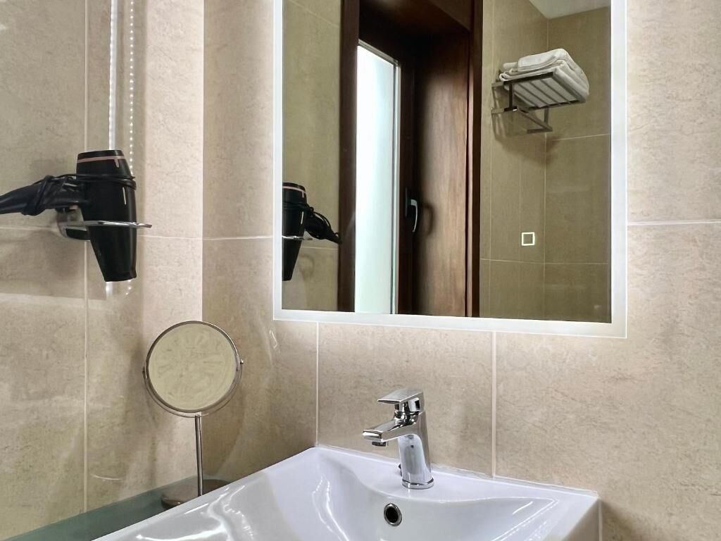 Une salle de bain avec un lavabo blanc, un miroir, un porte-serviettes et un sèche-cheveux.