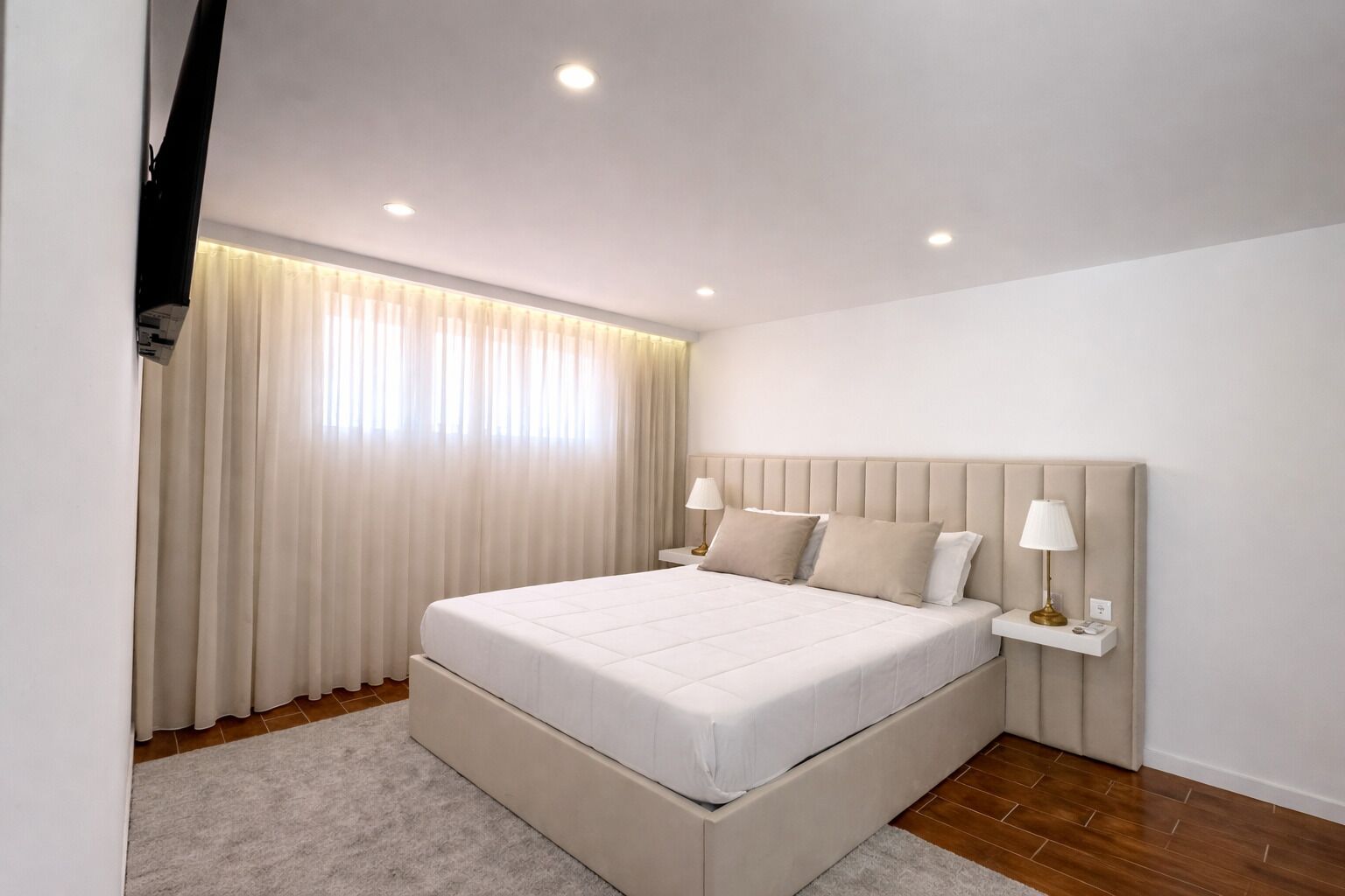 A modern bedroom with a large bed, bedside lamps, and a window with curtains.