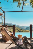 Uma pessoa relaxando em uma cadeira de praia com vista para um lago e montanhas.