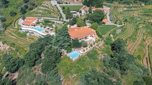 Eine Vogelperspektive eines Weinbergs mit terrassenförmigen Feldern, einem Schwimmbad und mehreren Gebäuden mit roten Ziegeldächern.
