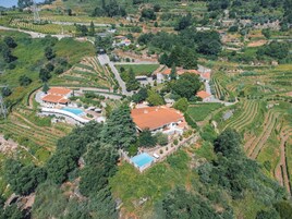 Vista aérea de um vinhedo com campos em socalcos, uma piscina e vários edifícios com telhados de terracota.