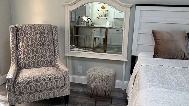 A bedroom with a bed, a vanity with a mirror, a chair, and a small stool. - Private • Peaceful Studio • Great Location (Lehigh Acres)