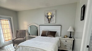 A bedroom with a bed, a chair, a nightstand, a lamp, and a wall-mounted artwork. - Private • Peaceful Studio • Great Location (Lehigh Acres)