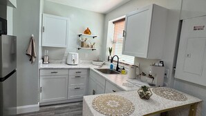 A compact kitchen with white cabinets, a refrigerator, a sink, and a dining area with a table and two chairs. - Private • Peaceful Studio • Great Location (Lehigh Acres)