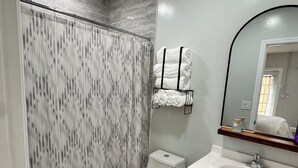 A bathroom with a toilet, a sink, a mirror, and a shower curtain. - Private • Peaceful Studio • Great Location (Lehigh Acres)