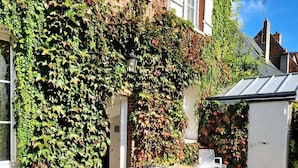 A patio with a table and chairs, surrounded by a brick wall with ivy. - “Le Secret des Cordelières” Cottage – Charming Character Residence in Normandy (Neufchâtel-en-Bray)