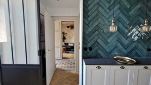 A kitchen with a herringbone tile backsplash, pendant lights, and a black countertop. - “Le Secret des Cordelières” Cottage – Charming Character Residence in Normandy (Neufchâtel-en-Bray)