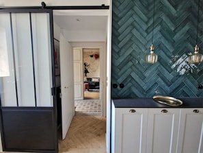 A kitchen with a herringbone tile backsplash, pendant lights, and a black countertop. - “Le Secret des Cordelières” Cottage – Charming Character Residence in Normandy (Neufchâtel-en-Bray)