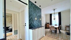 A modern kitchen with a herringbone backsplash, a dining area with a patterned rug, and a view into another room. - “Le Secret des Cordelières” Cottage – Charming Character Residence in Normandy (Neufchâtel-en-Bray)
