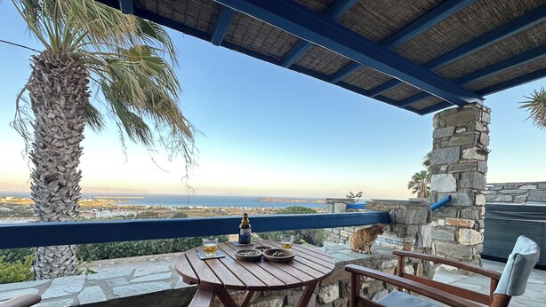 Une table en bois avec une bouteille et des verres, un pilier de pierre et une vue sur la mer.