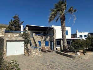 A stone building with blue shutters, a white garage, and a palm tree. - Villa Drionisi in Tzanes, Paros · 6 Guests (Tzanes)