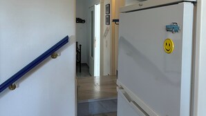 Un couloir avec un réfrigérateur blanc, une rambarde bleue et un escalier menant à une autre pièce.