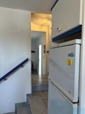 A hallway with a white refrigerator, a blue railing, and a staircase leading to another room. - Villa Drionisi in Tzanes, Paros · 6 Guests (Tzanes)