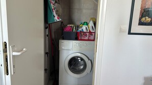 Une buanderie équipée d’un lave-linge, d’un panier à linge rouge et d’une étagère contenant des produits de nettoyage.