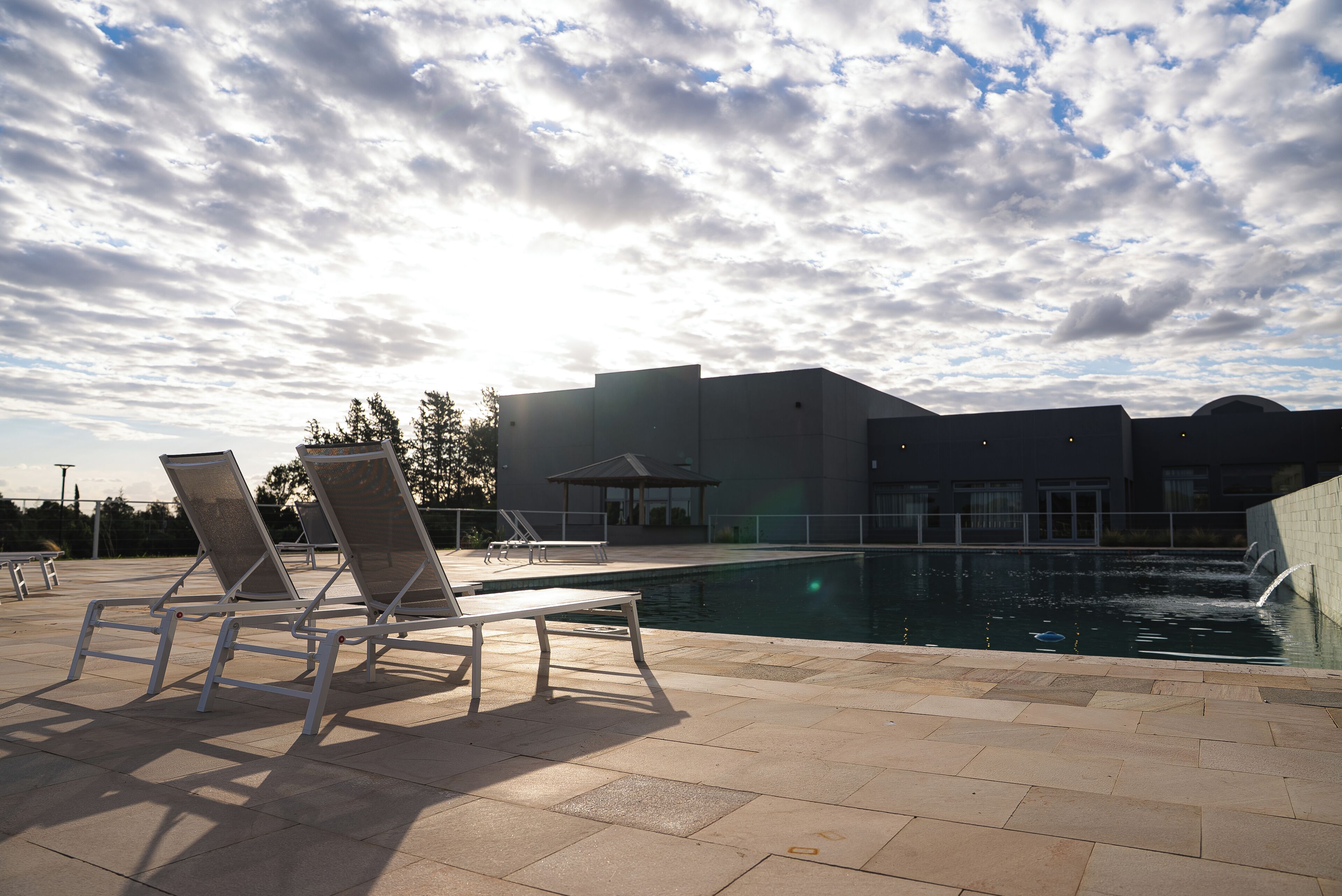 Una piscina con sillones de descanso, un edificio al fondo y un cielo nublado.