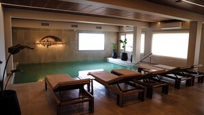 Un área de piscina con sillones de descanso, un accesorio de luz fijado a la pared y ventanas amplias.