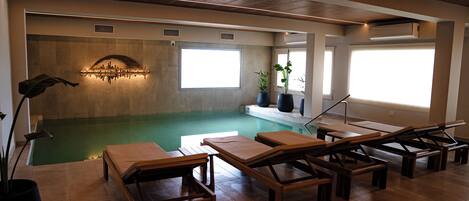 A pool area with lounge chairs, a wall-mounted light fixture, and large windows.