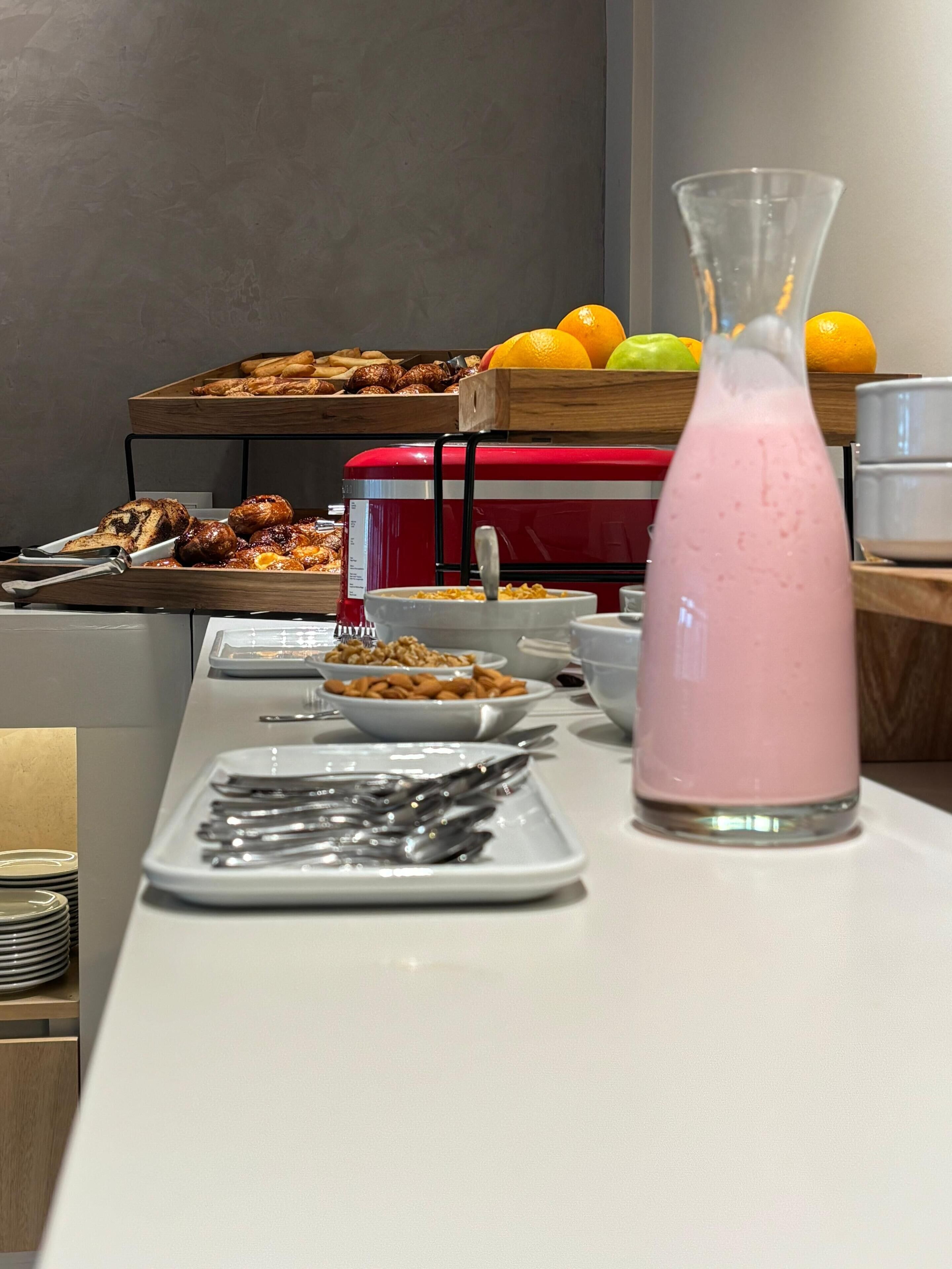 A buffet setup with various food items, a pink beverage, and a fruit display.