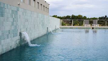 A swimming pool with water jets, a tiled wall, and a building in the background.