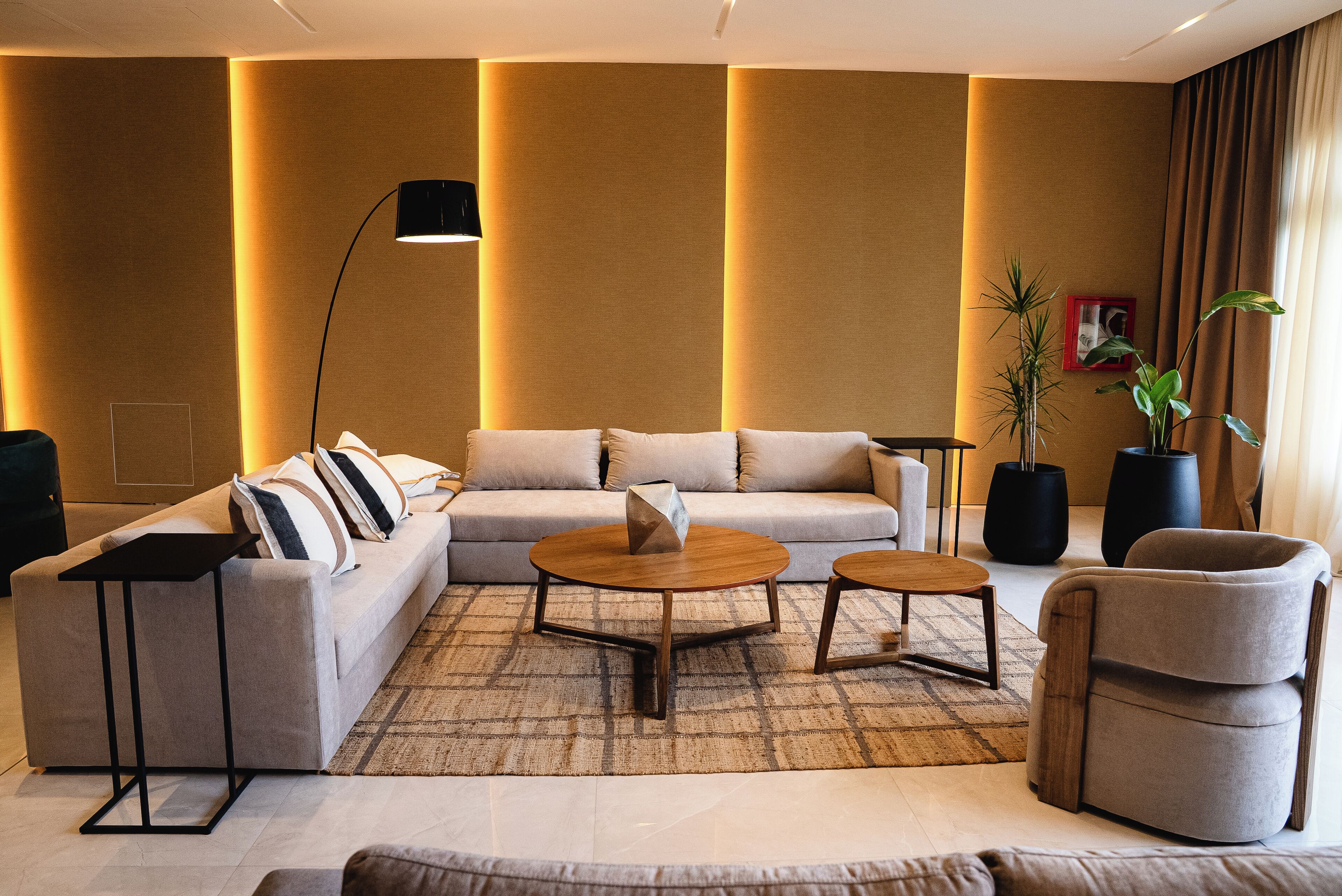 A modern living room with a sectional sofa, two round coffee tables, a floor lamp, and a potted plant.