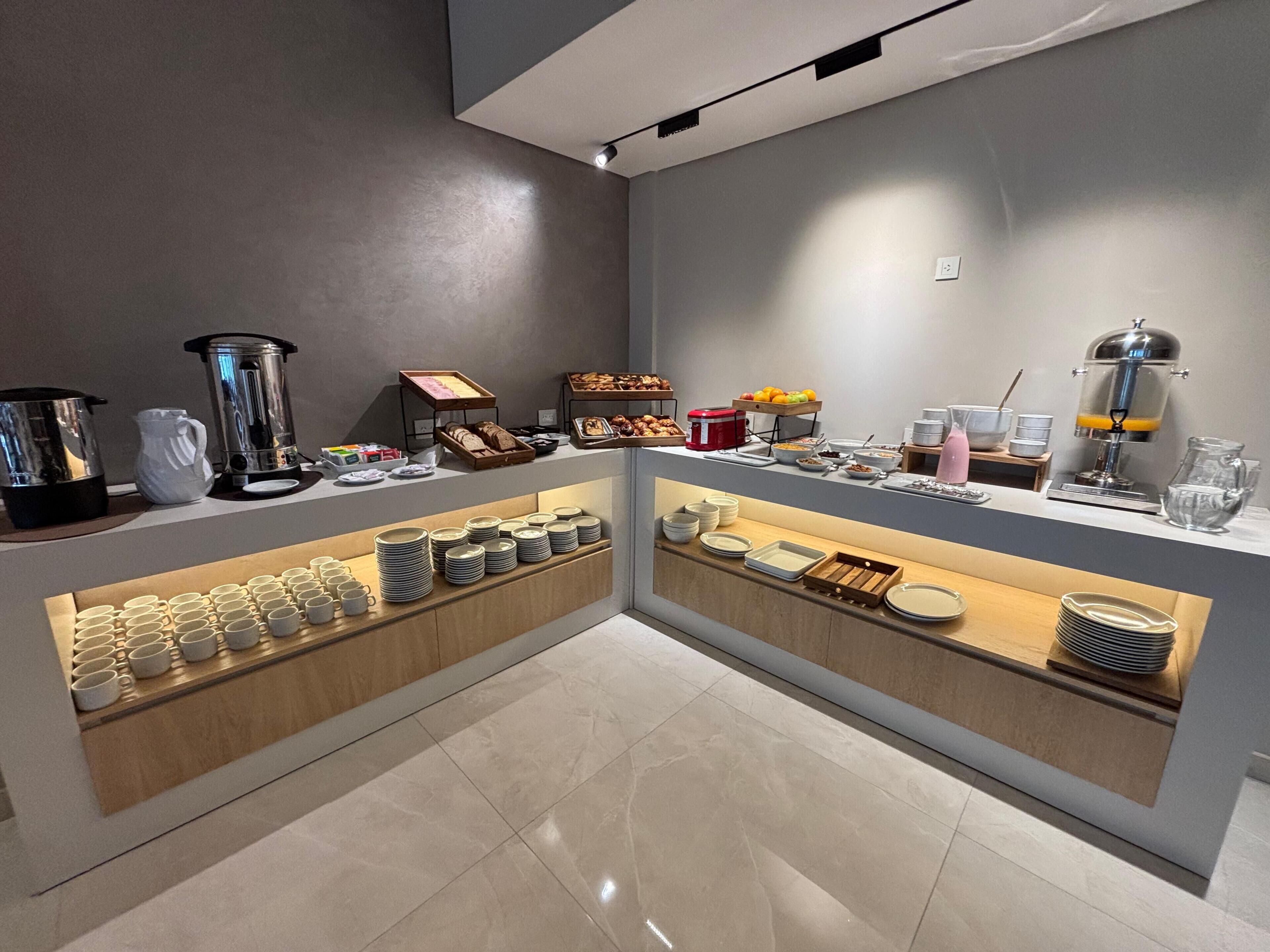 Un bufé de desayuno con diversas opciones de alimentos y bebidas, una máquina de café y una presentación de frutas.
